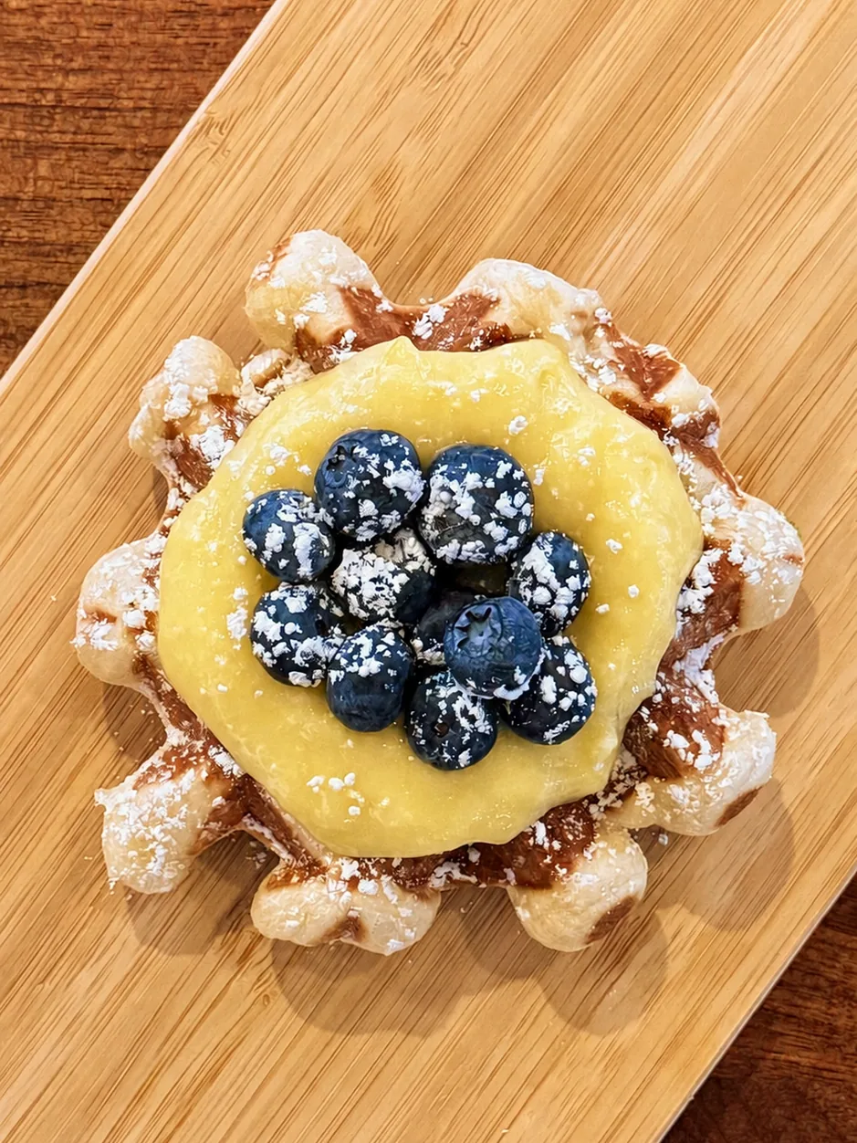 A blueberry-topped waffle on a wooden serving board