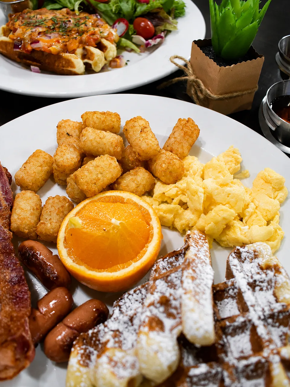 A brunch plate with waffles, eggs, potatoes, sausages and orange