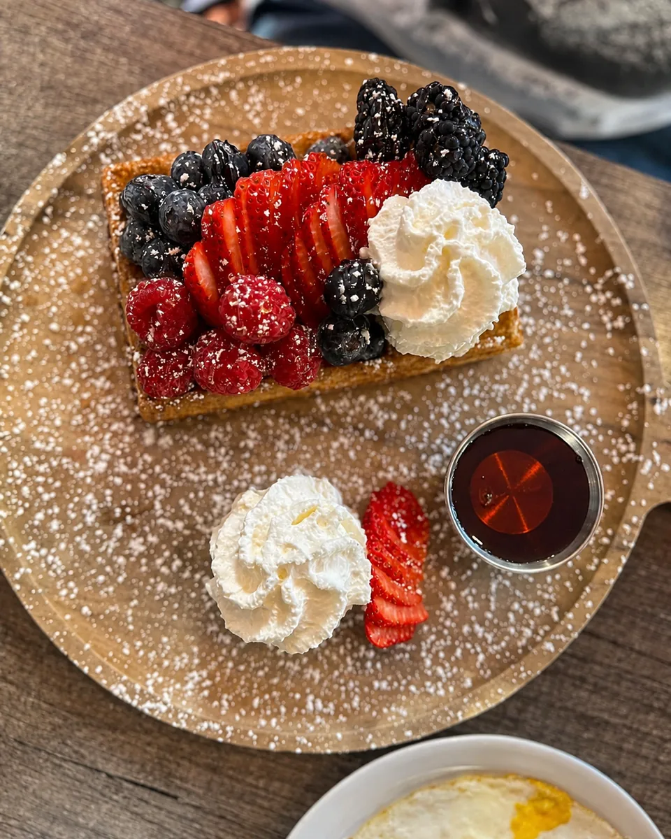 A golden waffle topped with strawberries, blueberries, blackberries, raspberries and whipped cream